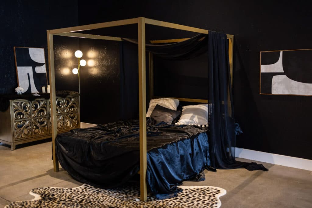 Sophisticated event rental space in Oklahoma, featuring a luxurious black canopy bed with gold accents, complemented by modern art and moody lighting.