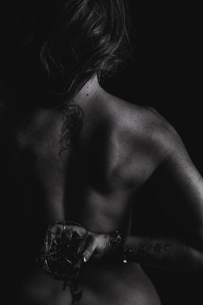 Black and white branding photography of a woman holding a glass behind her back, emphasizing a tattoo and showcasing bartending or beverage services.