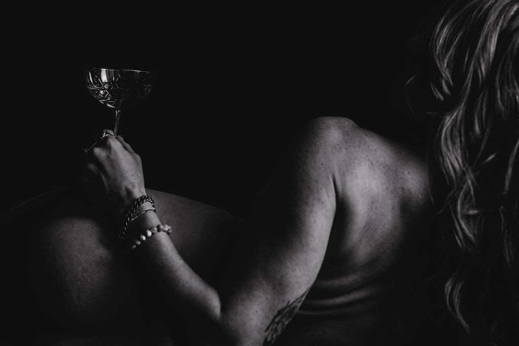 Black and white branding photography of a woman reclining with a glass in hand, showcasing bartending services in an elegant and mysterious pose.