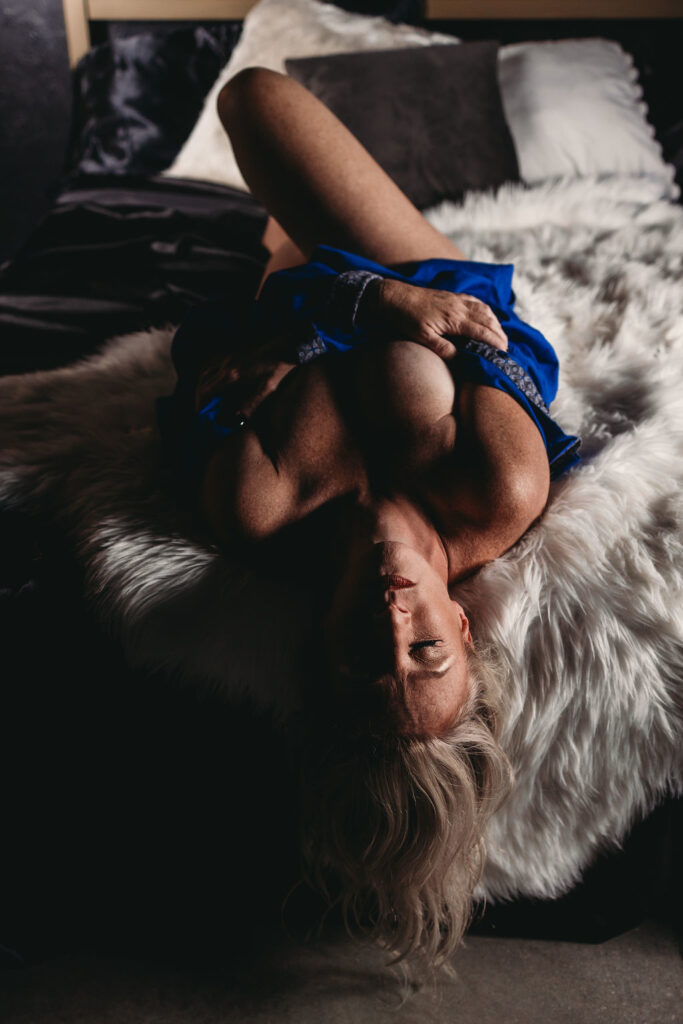 Woman lying on a plush bed during an empowering boudoir photography session.